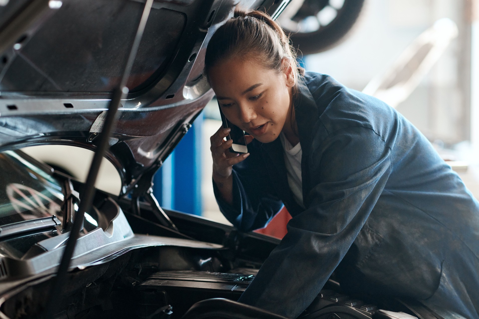 Foto de una mecánica hablando por su teléfono celular mientras trabajaba en un taller de reparación de automóviles